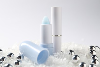 Photo of Moisturizing lip balms and Christmas decor on artificial snow against white background, closeup. Winter care