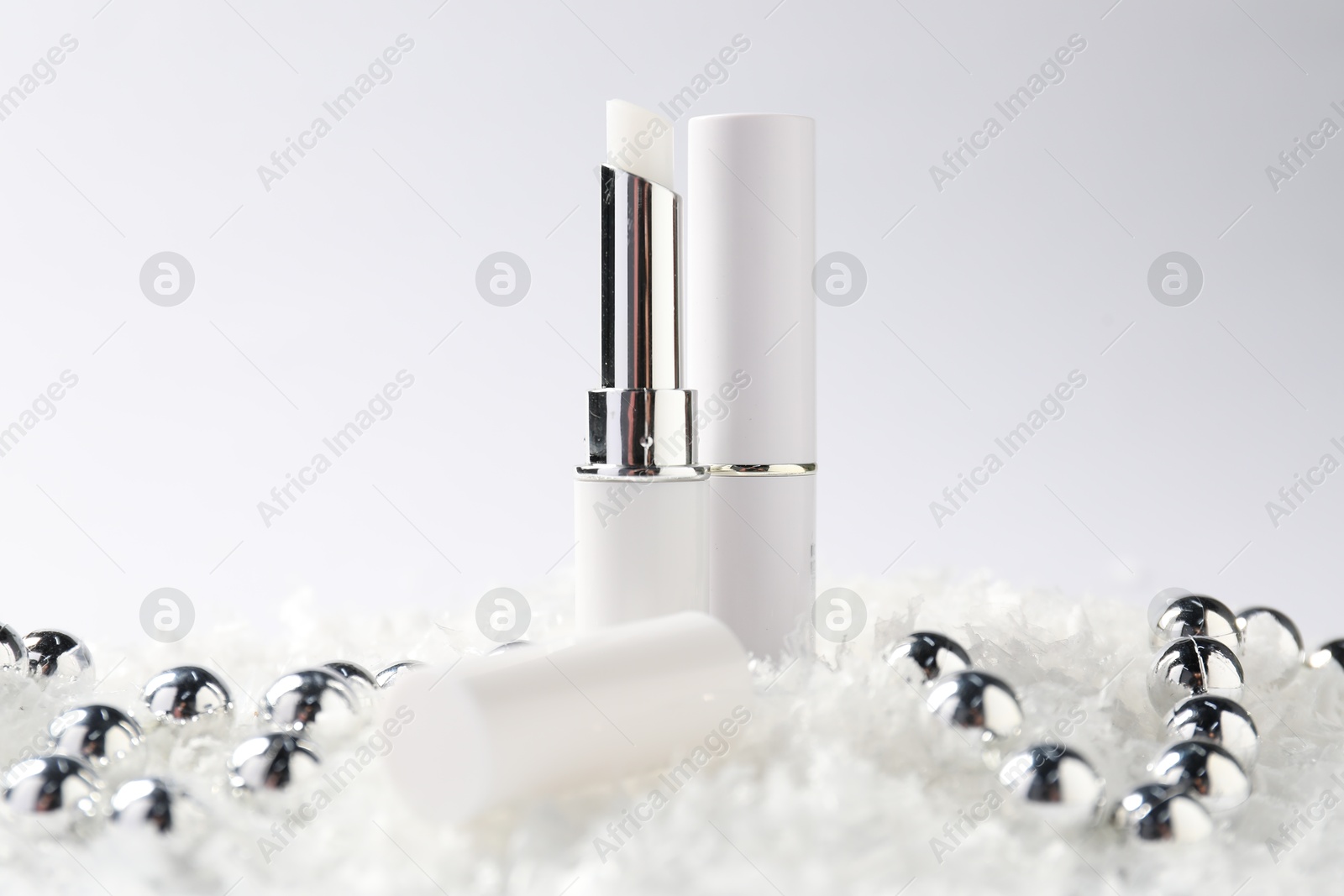 Moisturizing lip balms and Christmas decor on artificial snow against white background, closeup. Winter care Photo of Moisturizing lip balms and Christmas decor on artificial snow against white background, closeup. Winter care