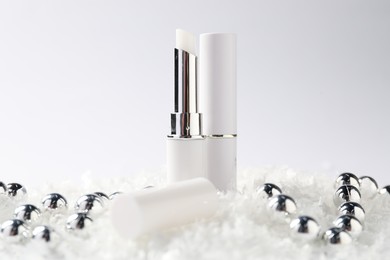 Photo of Moisturizing lip balms and Christmas decor on artificial snow against white background, closeup. Winter care