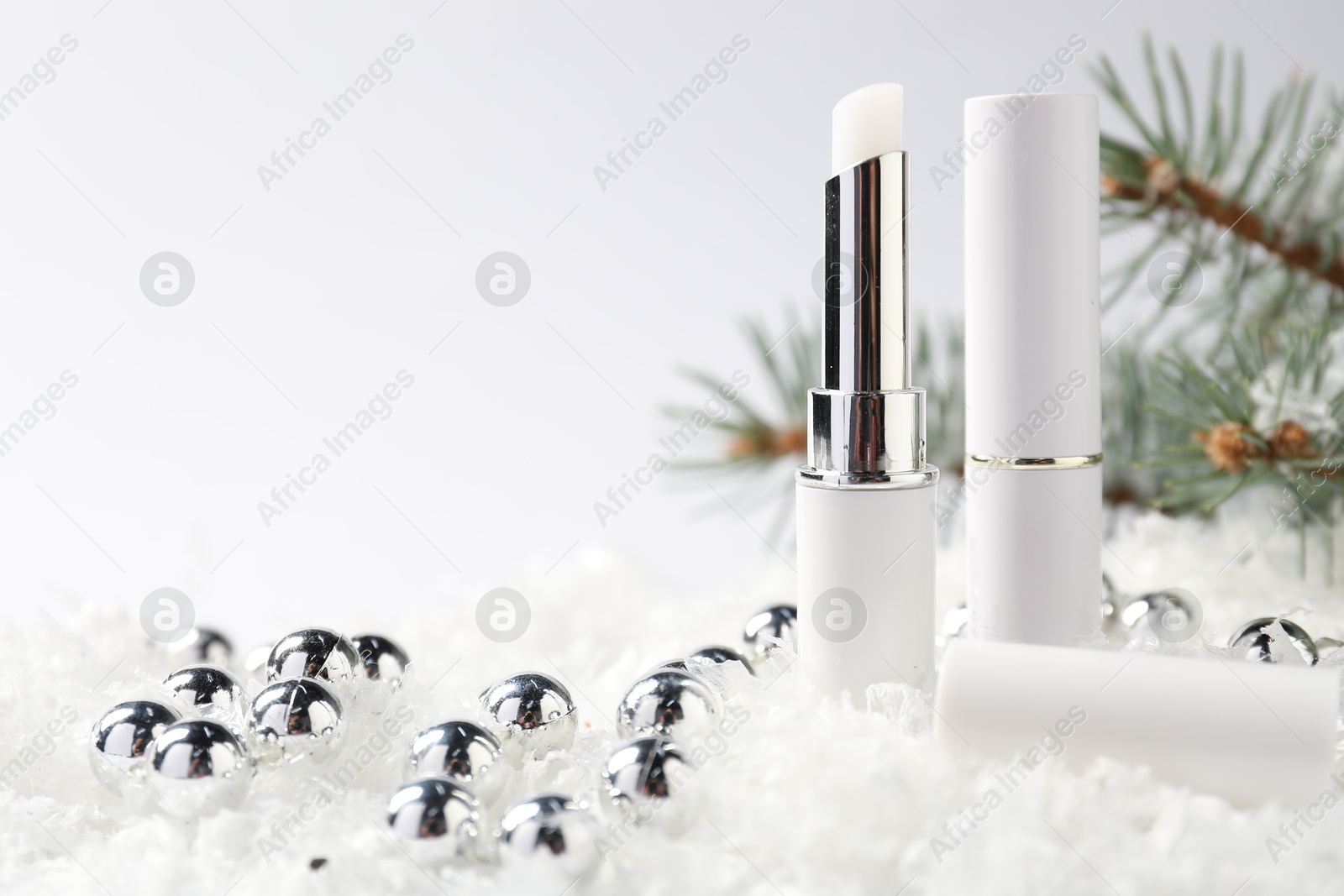 Moisturizing lip balms, Christmas decor and fir tree branches on artificial snow against white background, closeup. Space for text Photo of Moisturizing lip balms, Christmas decor and fir tree branches on artificial snow against white background, closeup. Space for text