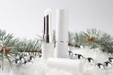 Photo of Moisturizing lip balms, Christmas decor and fir tree branches on artificial snow against white background, closeup. Winter care