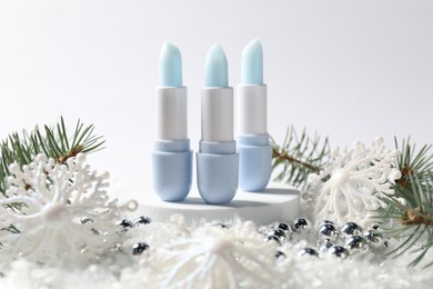 Photo of Moisturizing lip balms, Christmas decor and fir tree branches on artificial snow against white background, closeup. Winter care