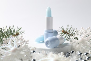 Photo of Moisturizing lip balms, Christmas decor and fir tree branches on artificial snow against white background, closeup. Winter care