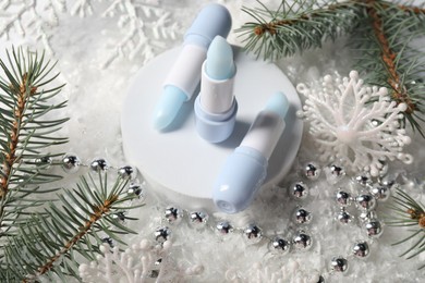 Photo of Moisturizing lip balms, Christmas decor and fir tree branches on artificial snow, closeup. Winter care