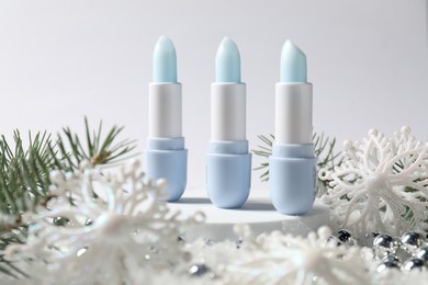 Photo of Moisturizing lip balms, Christmas decor and fir tree branches on artificial snow against white background, closeup. Winter care