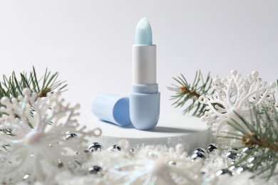 Photo of Moisturizing lip balm, Christmas decor and fir tree branches on artificial snow against white background, closeup. Winter care