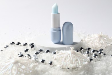 Photo of Moisturizing lip balm and Christmas decor on artificial snow against white background, closeup. Winter care
