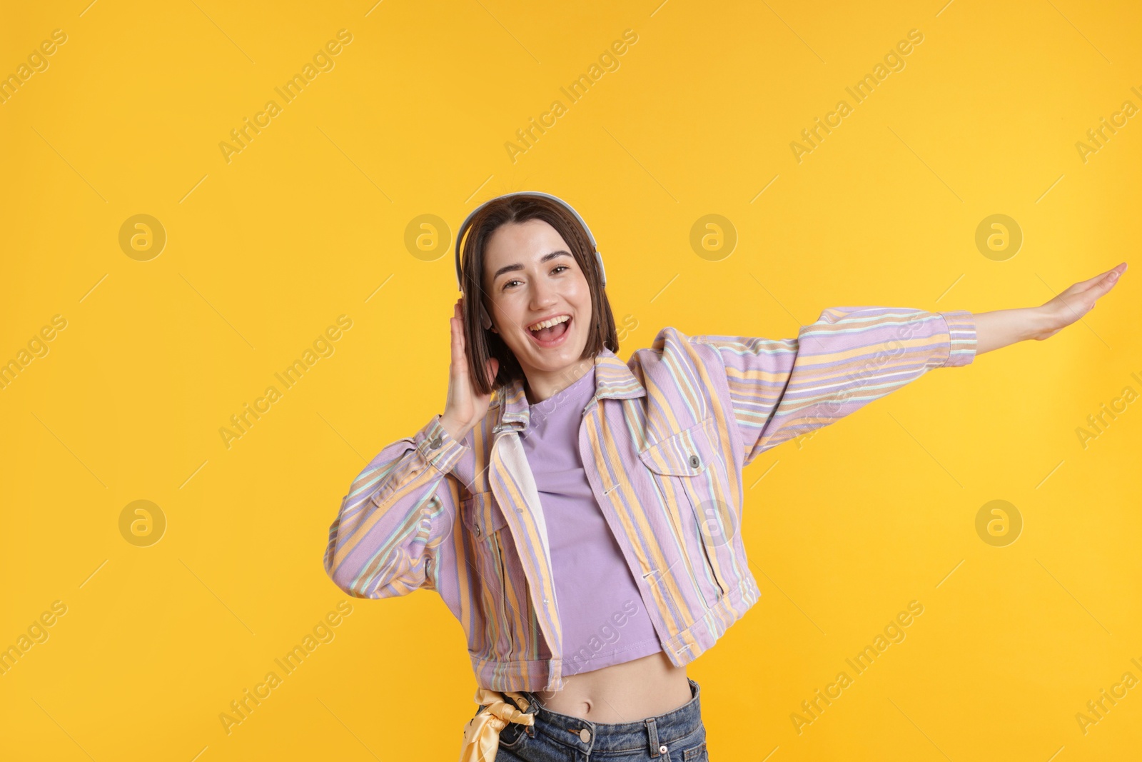 Happy woman in headphones dancing on yellow background Photo of Happy woman in headphones dancing on yellow background