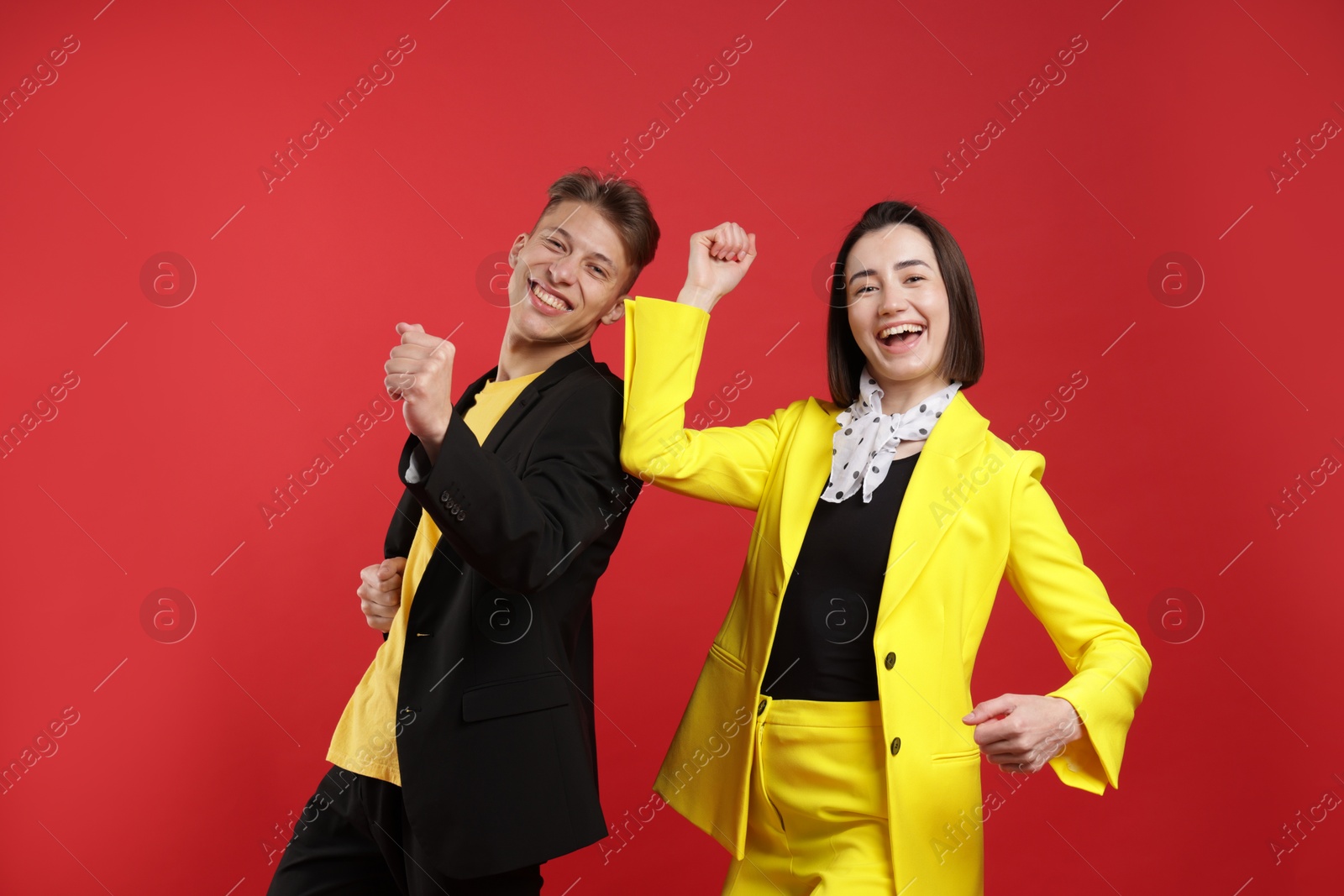 Happy couple in stylish clothes dancing on red background Photo of Happy couple in stylish clothes dancing on red background