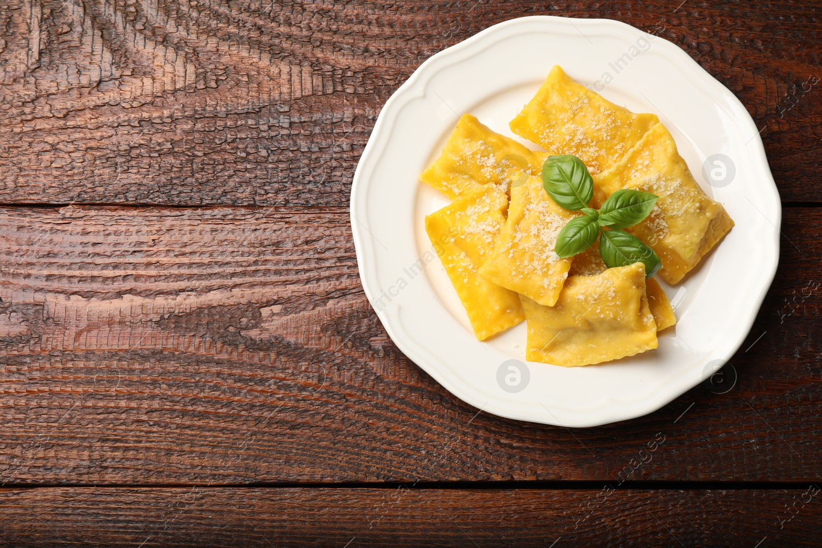 Delicious ravioli with parmesan cheese and basil on wooden table, top view. Space for text Photo of Delicious ravioli with parmesan cheese and basil on wooden table, top view. Space for text