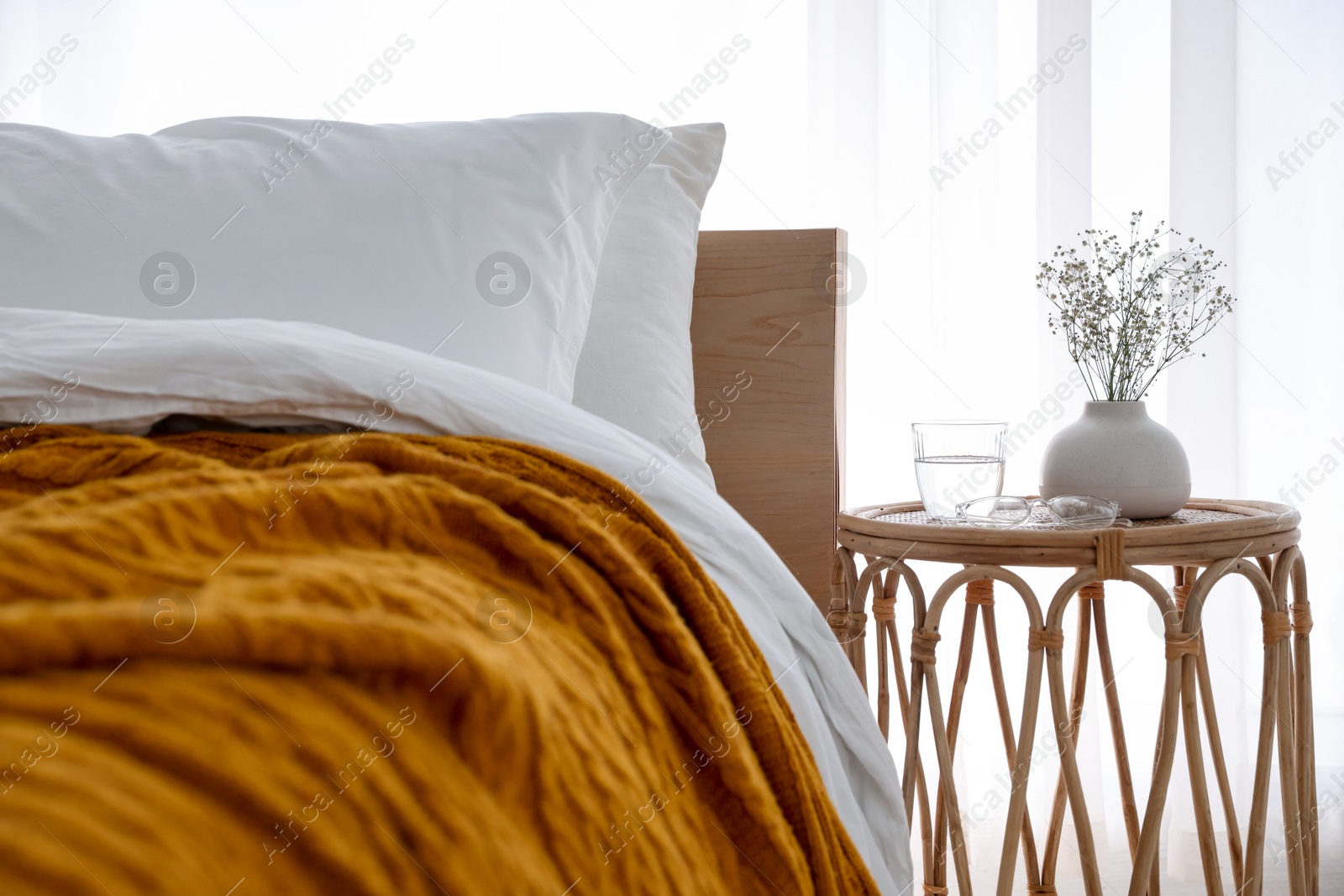 Bedside table with flowers in vase, glass of water and glasses near bed indoors Photo of Bedside table with flowers in vase, glass of water and glasses near bed indoors