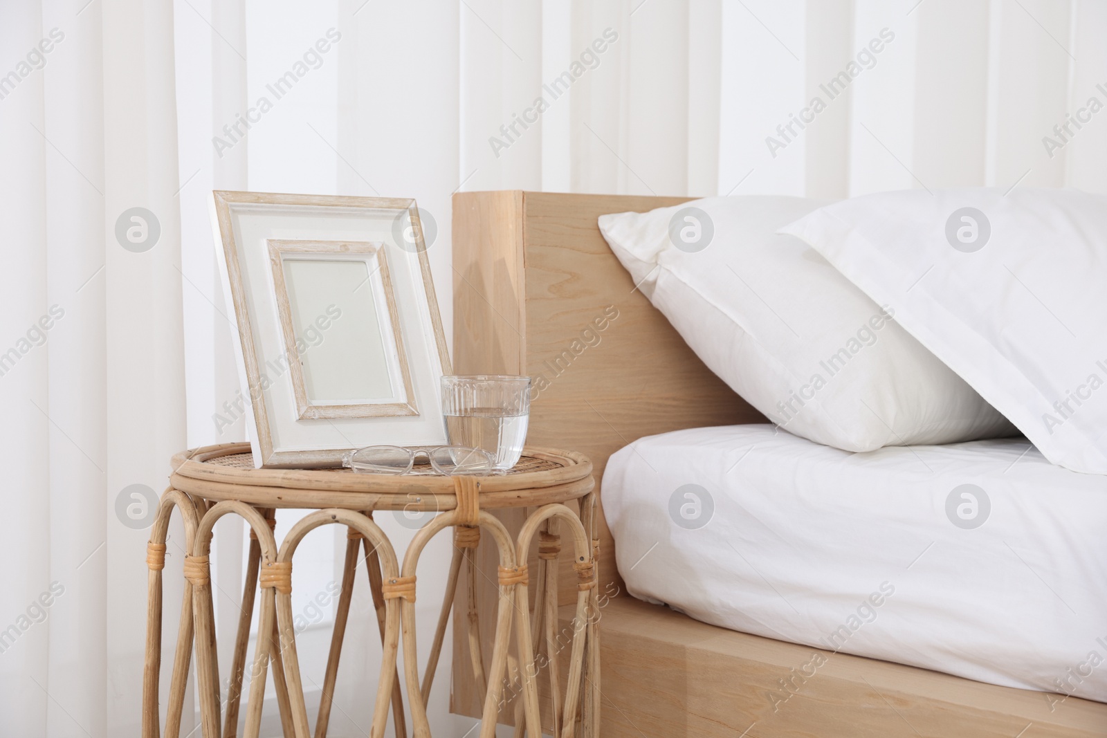 Bedside table with picture frame and glass of water near bed in room Photo of Bedside table with picture frame and glass of water near bed in room
