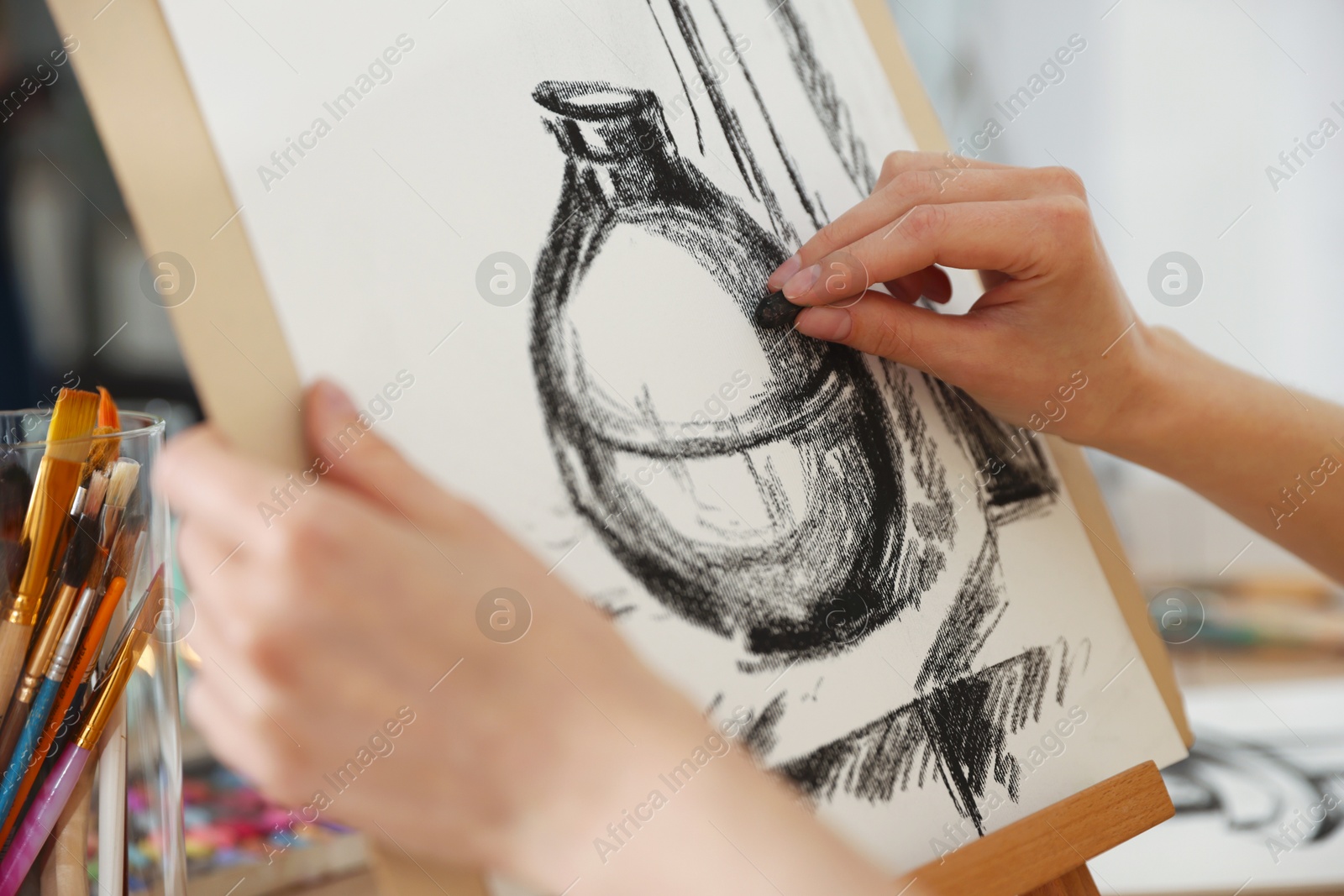 Woman drawing picture with black wax crayon on easel at table in artist's studio, closeup Photo of Woman drawing picture with black wax crayon on easel at table in artist's studio, closeup