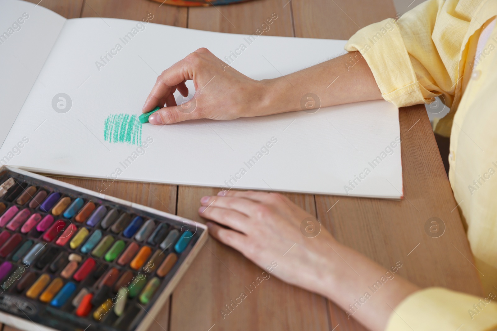 Woman drawing picture with bright wax crayons on paper at wooden table in artist's studio, closeup Photo of Woman drawing picture with bright wax crayons on paper at wooden table in artist's studio, closeup