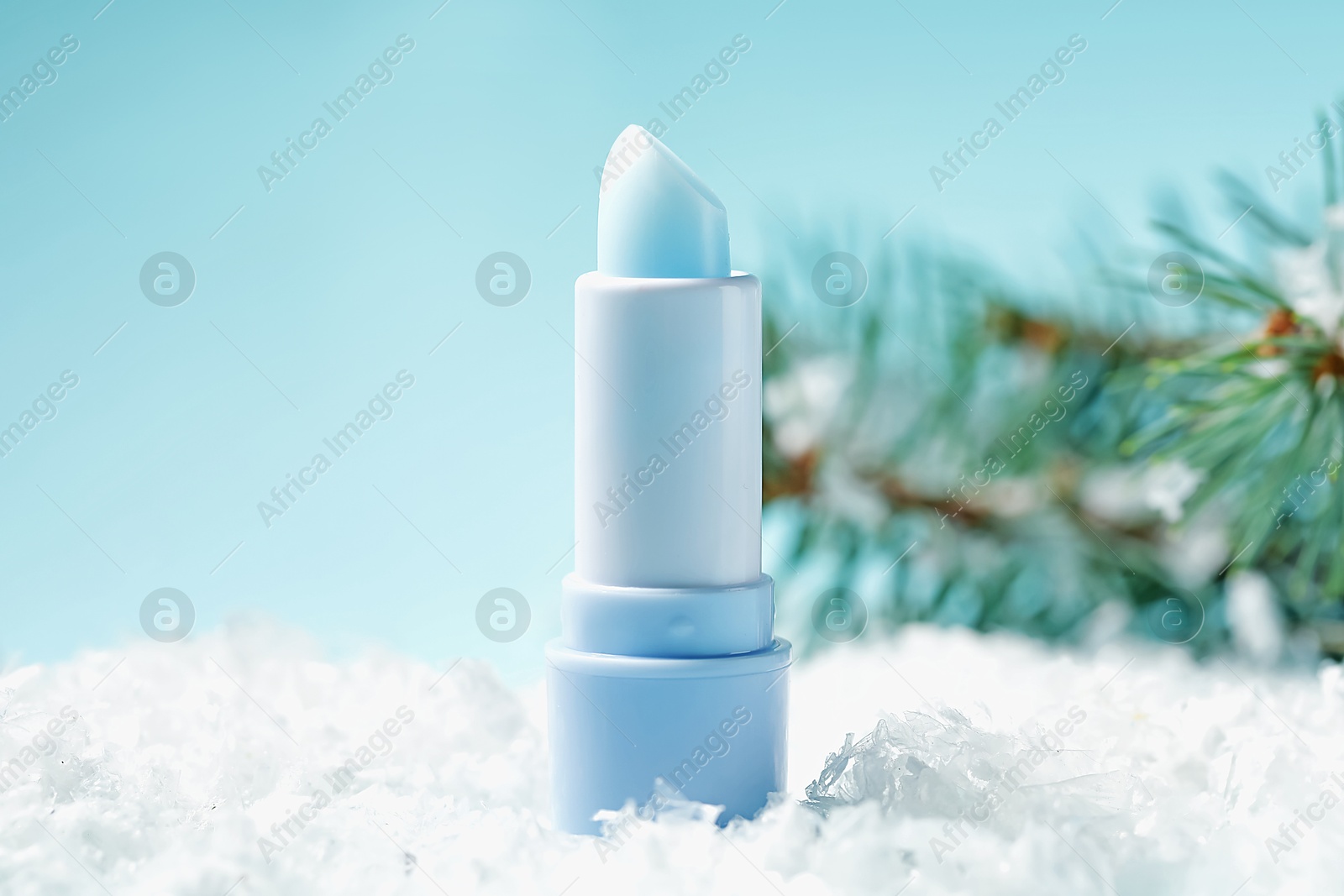 Moisturizing lip balm and fir tree branches on artificial snow against light blue background, closeup. Winter care Photo of Moisturizing lip balm and fir tree branches on artificial snow against light blue background, closeup. Winter care