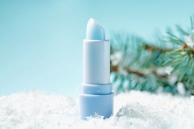 Photo of Moisturizing lip balm and fir tree branches on artificial snow against light blue background, closeup. Winter care