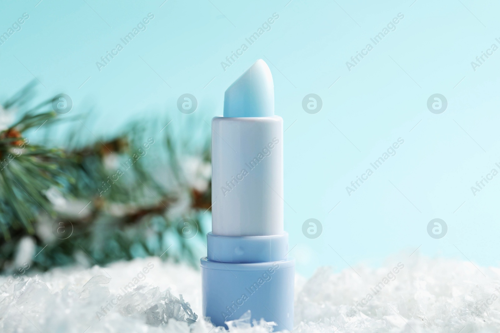 Moisturizing lip balm and fir tree branches on artificial snow against light blue background, closeup. Winter care Photo of Moisturizing lip balm and fir tree branches on artificial snow against light blue background, closeup. Winter care