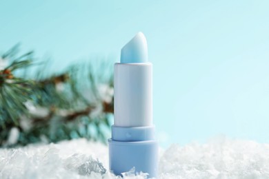Photo of Moisturizing lip balm and fir tree branches on artificial snow against light blue background, closeup. Winter care