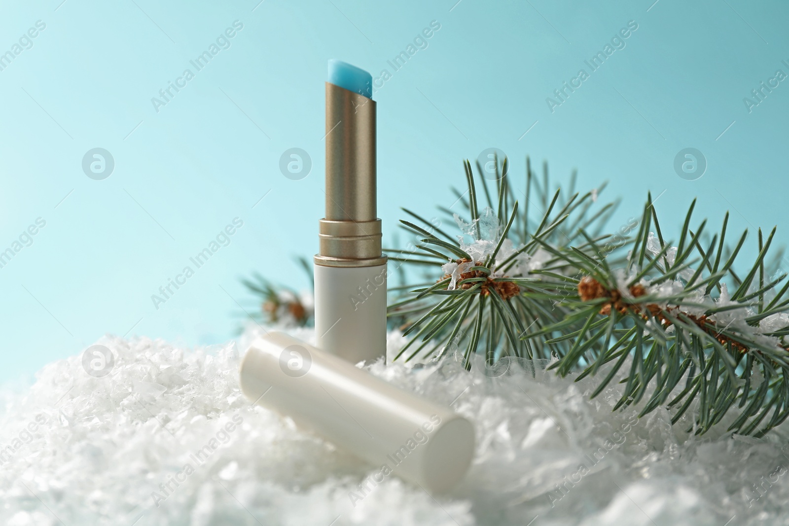 Moisturizing lip balm and fir tree branches on artificial snow against light blue background, closeup. Winter care Photo of Moisturizing lip balm and fir tree branches on artificial snow against light blue background, closeup. Winter care