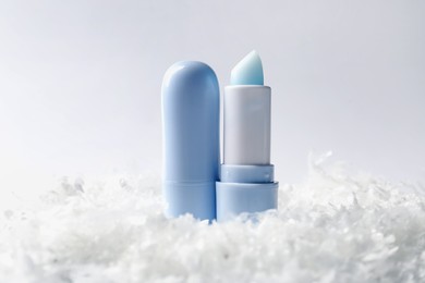 Photo of Moisturizing lip balms on artificial snow against white background, closeup. Winter care