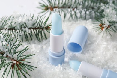 Photo of Moisturizing lip balms and fir tree branches on artificial snow, closeup. Winter care