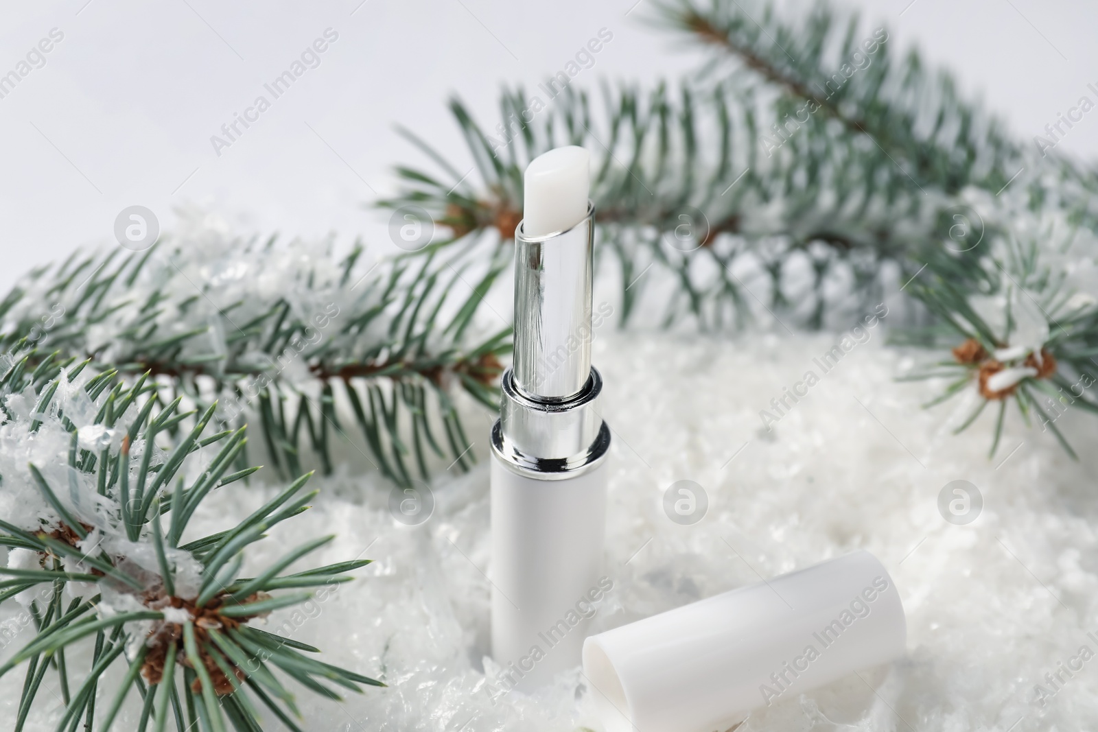 Moisturizing lip balm and fir tree branches on artificial snow against white background, closeup. Winter care Photo of Moisturizing lip balm and fir tree branches on artificial snow against white background, closeup. Winter care