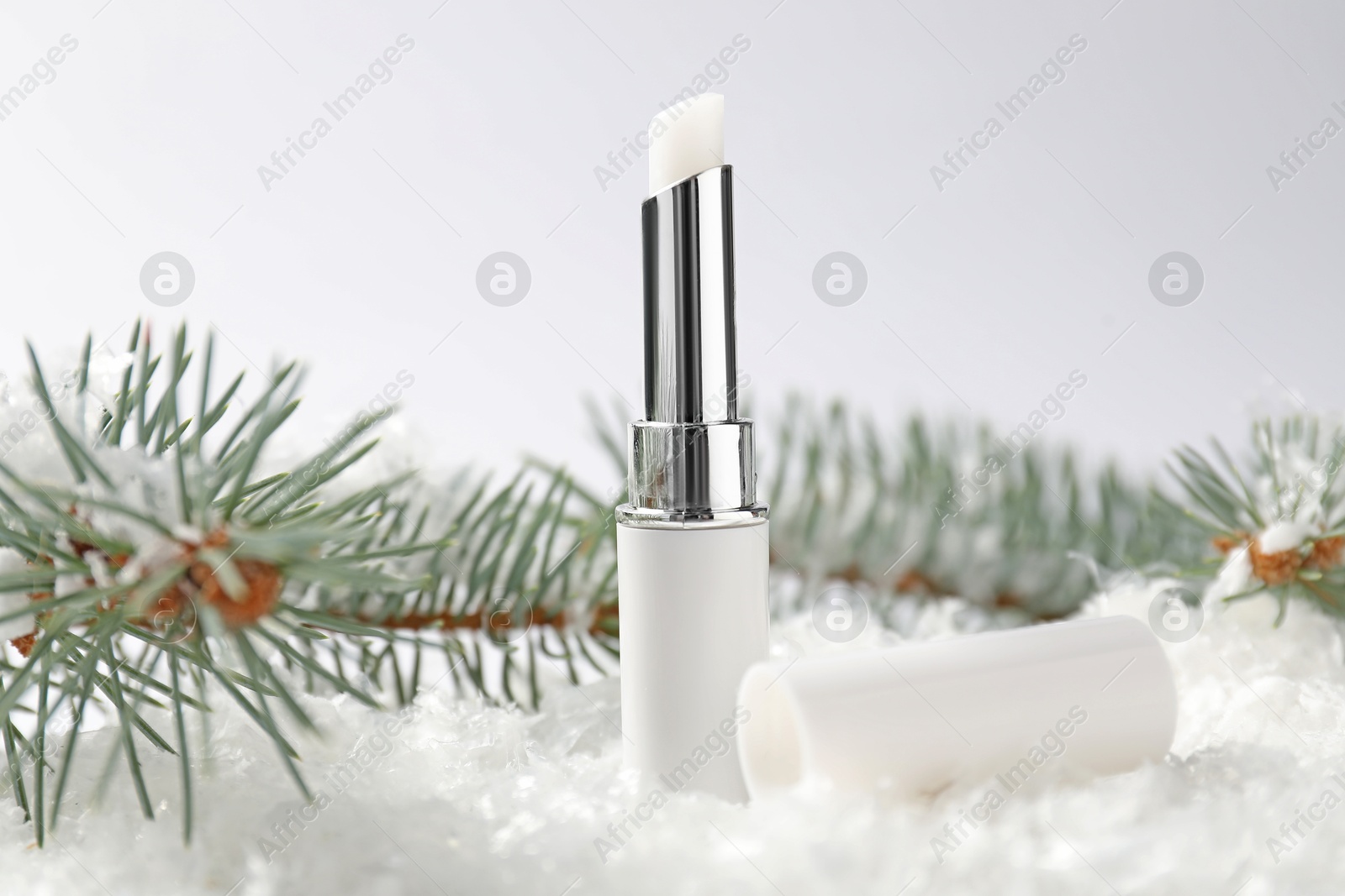Moisturizing lip balm and fir tree branches on artificial snow against white background, closeup. Winter care Photo of Moisturizing lip balm and fir tree branches on artificial snow against white background, closeup. Winter care