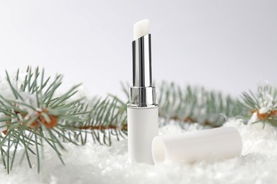 Photo of Moisturizing lip balm and fir tree branches on artificial snow against white background, closeup. Winter care