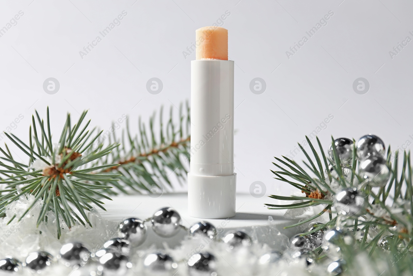 Moisturizing lip balm, Christmas decor and fir tree branches on artificial snow against white background, closeup. Winter care Photo of Moisturizing lip balm, Christmas decor and fir tree branches on artificial snow against white background, closeup. Winter care