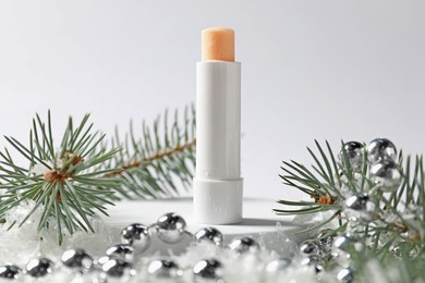 Photo of Moisturizing lip balm, Christmas decor and fir tree branches on artificial snow against white background, closeup. Winter care