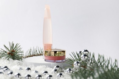 Photo of Moisturizing lip balms, Christmas decor and fir tree branches on artificial snow against white background, closeup. Winter care