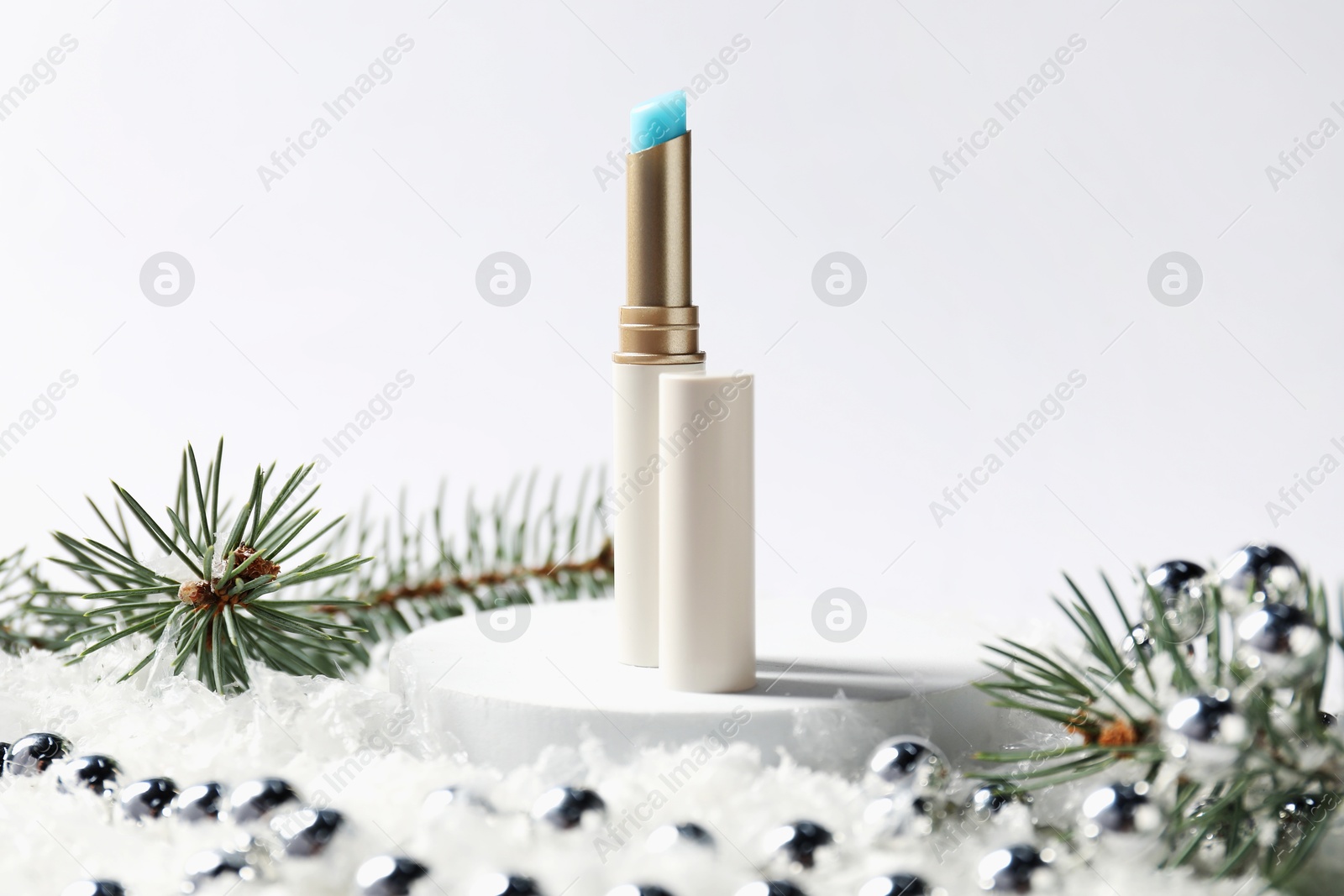 Photo of Moisturizing lip balm, Christmas decor and fir tree branches on artificial snow against white background, closeup. Winter care