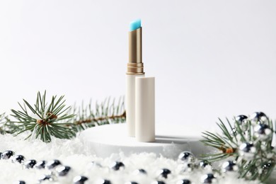 Photo of Moisturizing lip balm, Christmas decor and fir tree branches on artificial snow against white background, closeup. Winter care