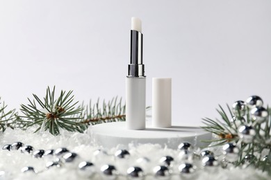 Photo of Moisturizing lip balm, Christmas decor and fir tree branches on artificial snow against white background, closeup. Winter care