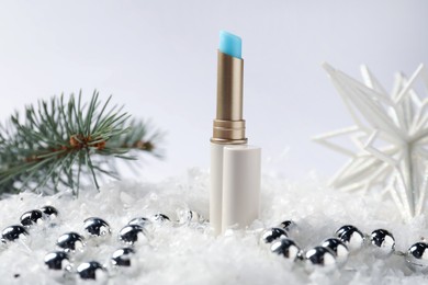 Photo of Moisturizing lip balm, Christmas decor and fir tree branches on artificial snow against white background, closeup. Winter care