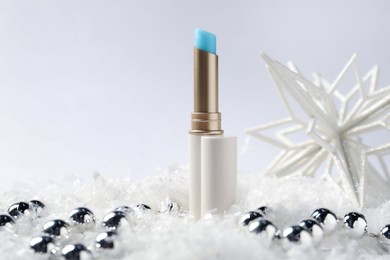 Photo of Moisturizing lip balm and Christmas decor on artificial snow against white background, closeup. Winter care
