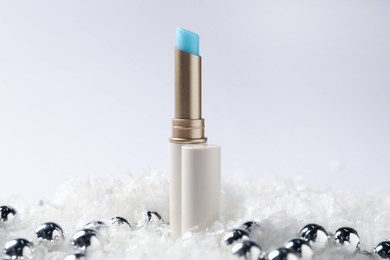 Photo of Moisturizing lip balm and Christmas decor on artificial snow against white background, closeup. Winter care