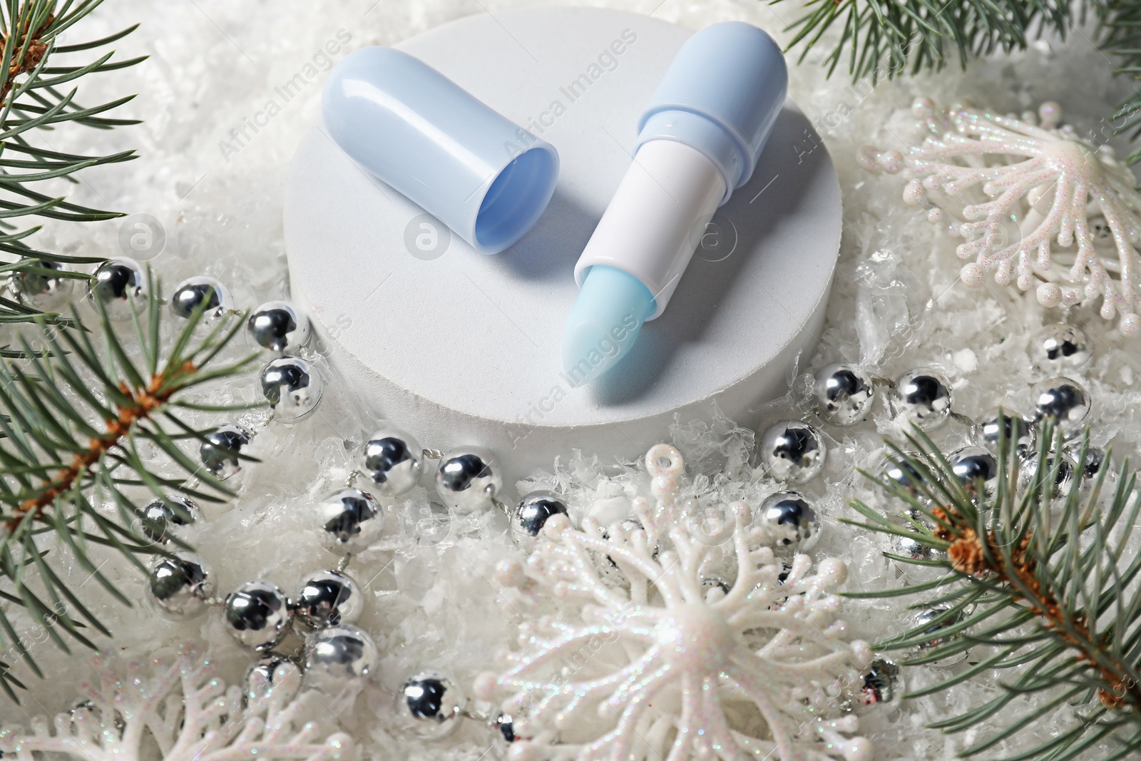 Moisturizing lip balm, Christmas decor and fir tree branches on artificial snow, closeup. Winter care Photo of Moisturizing lip balm, Christmas decor and fir tree branches on artificial snow, closeup. Winter care