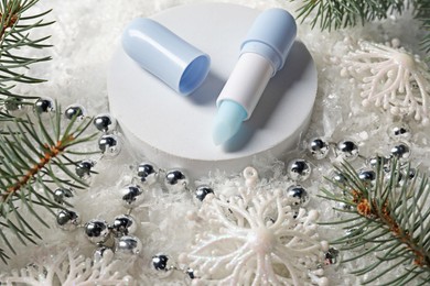 Photo of Moisturizing lip balm, Christmas decor and fir tree branches on artificial snow, closeup. Winter care