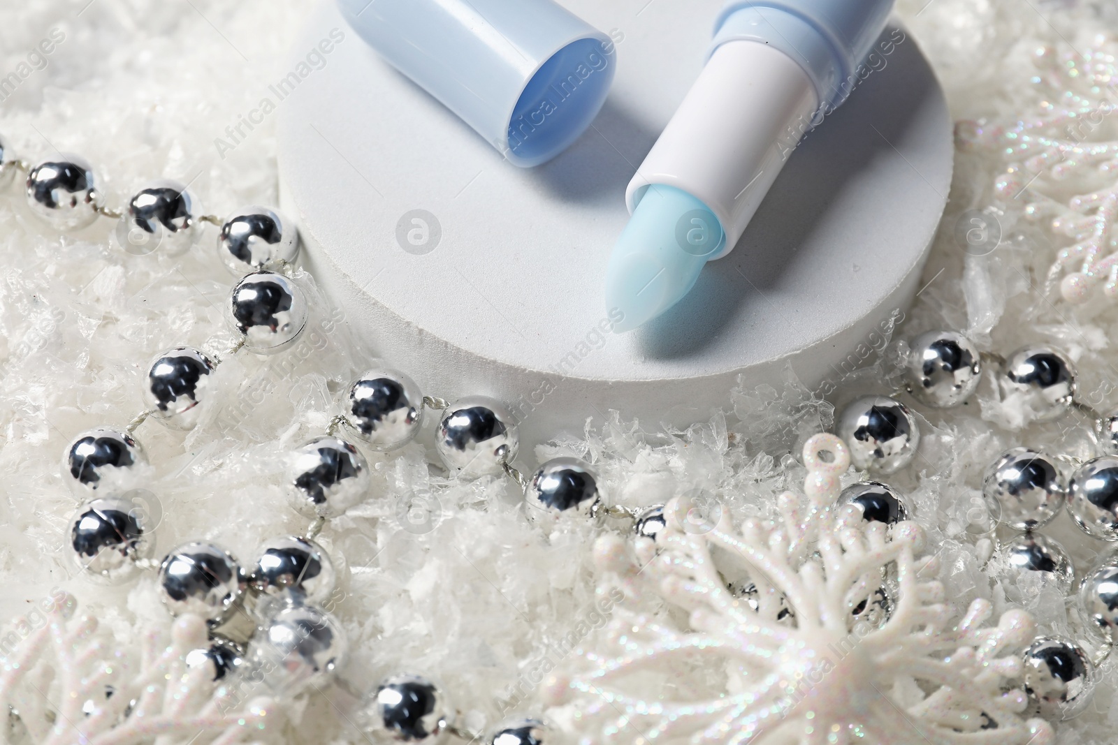 Moisturizing lip balm and Christmas decor on artificial snow, closeup. Winter care Photo of Moisturizing lip balm and Christmas decor on artificial snow, closeup. Winter care