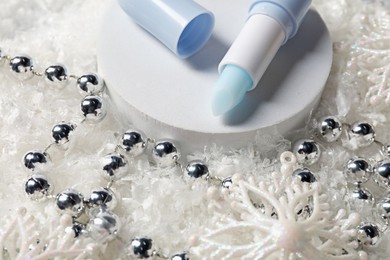 Photo of Moisturizing lip balm and Christmas decor on artificial snow, closeup. Winter care