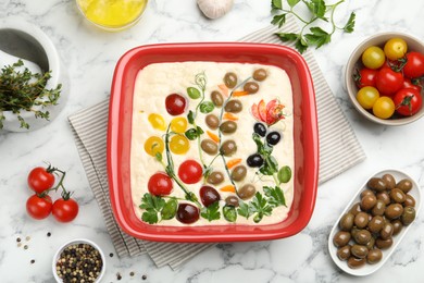 Photo of Raw focaccia with vegetables, olives and spices on white marble table, flat lay