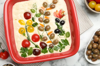 Photo of Raw focaccia with vegetables, olives and spices on white marble table, flat lay