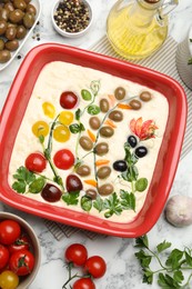 Photo of Raw focaccia with vegetables, olives and spices on white marble table, flat lay