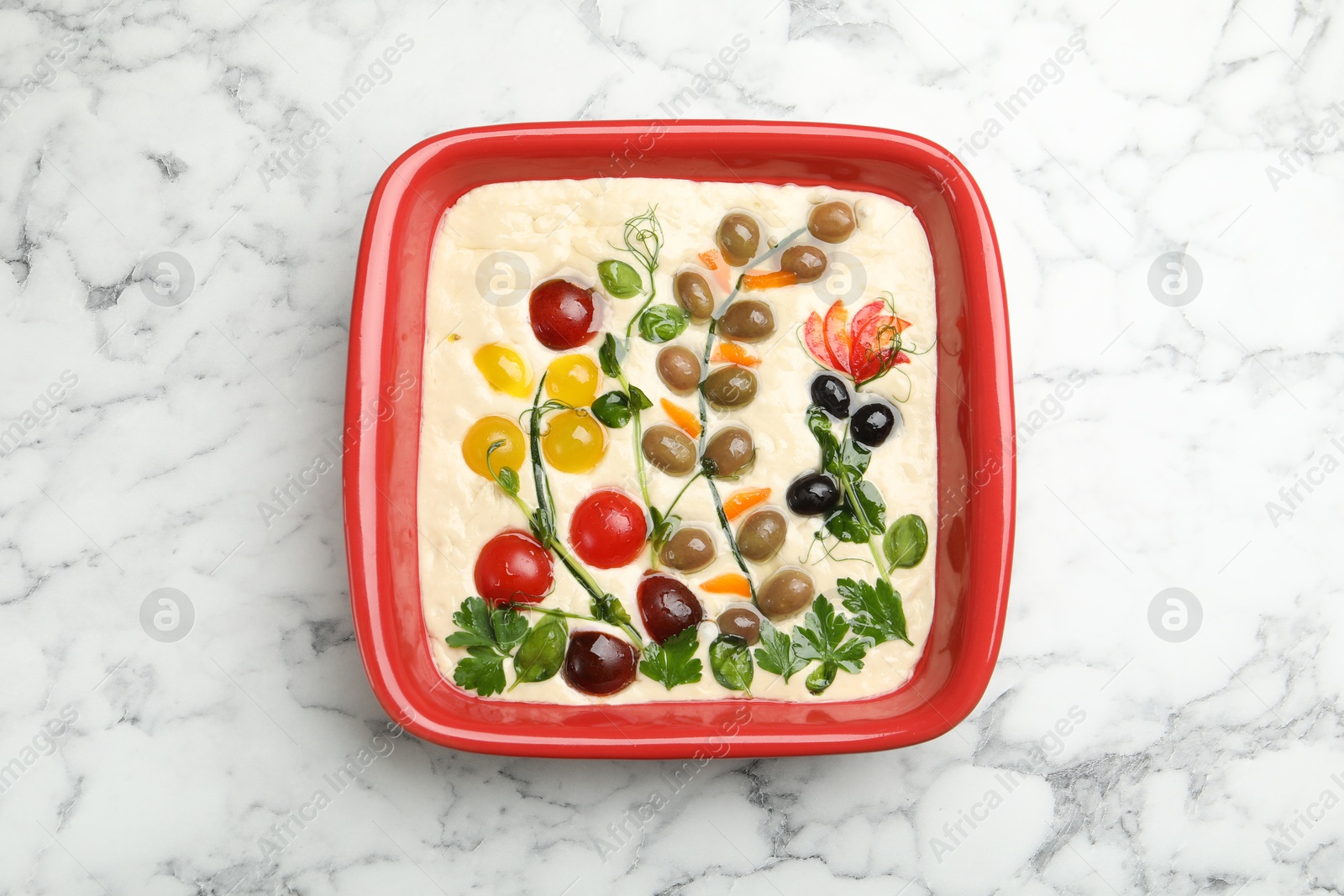 Raw focaccia with vegetables and olives in baking dish on white marble table, top view Photo of Raw focaccia with vegetables and olives in baking dish on white marble table, top view