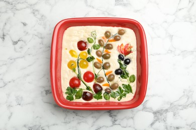Photo of Raw focaccia with vegetables and olives in baking dish on white marble table, top view
