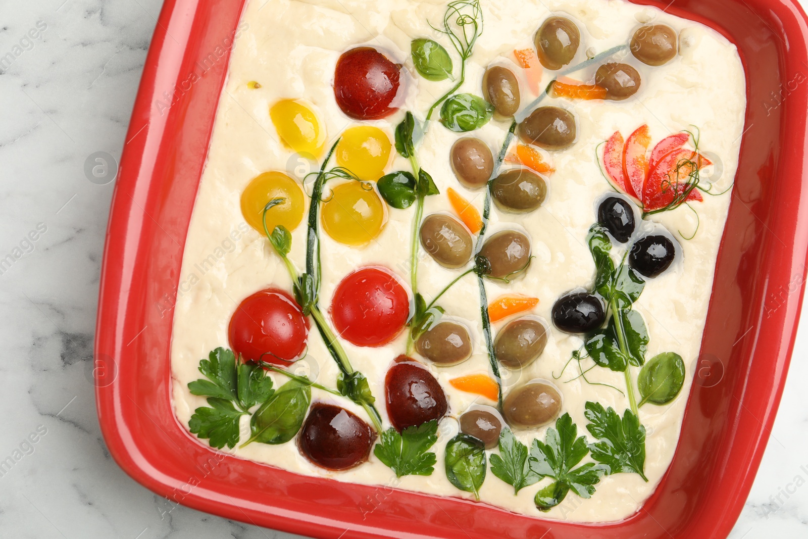 Raw focaccia with vegetables and olives in baking dish on white marble table, top view Photo of Raw focaccia with vegetables and olives in baking dish on white marble table, top view