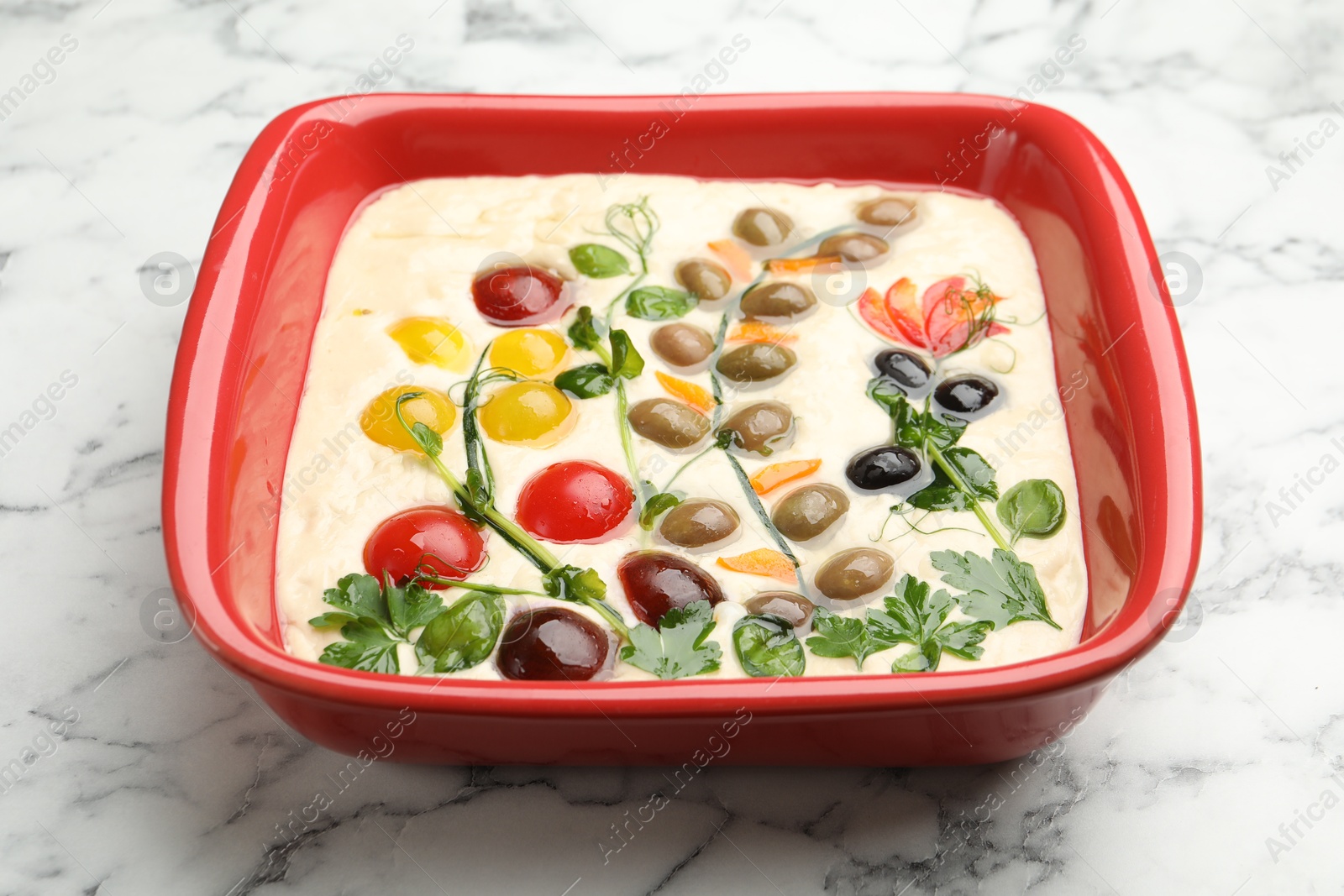 Raw focaccia with vegetables and olives in baking dish on white marble table, closeup Photo of Raw focaccia with vegetables and olives in baking dish on white marble table, closeup