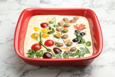 Photo of Raw focaccia with vegetables and olives in baking dish on white marble table, closeup