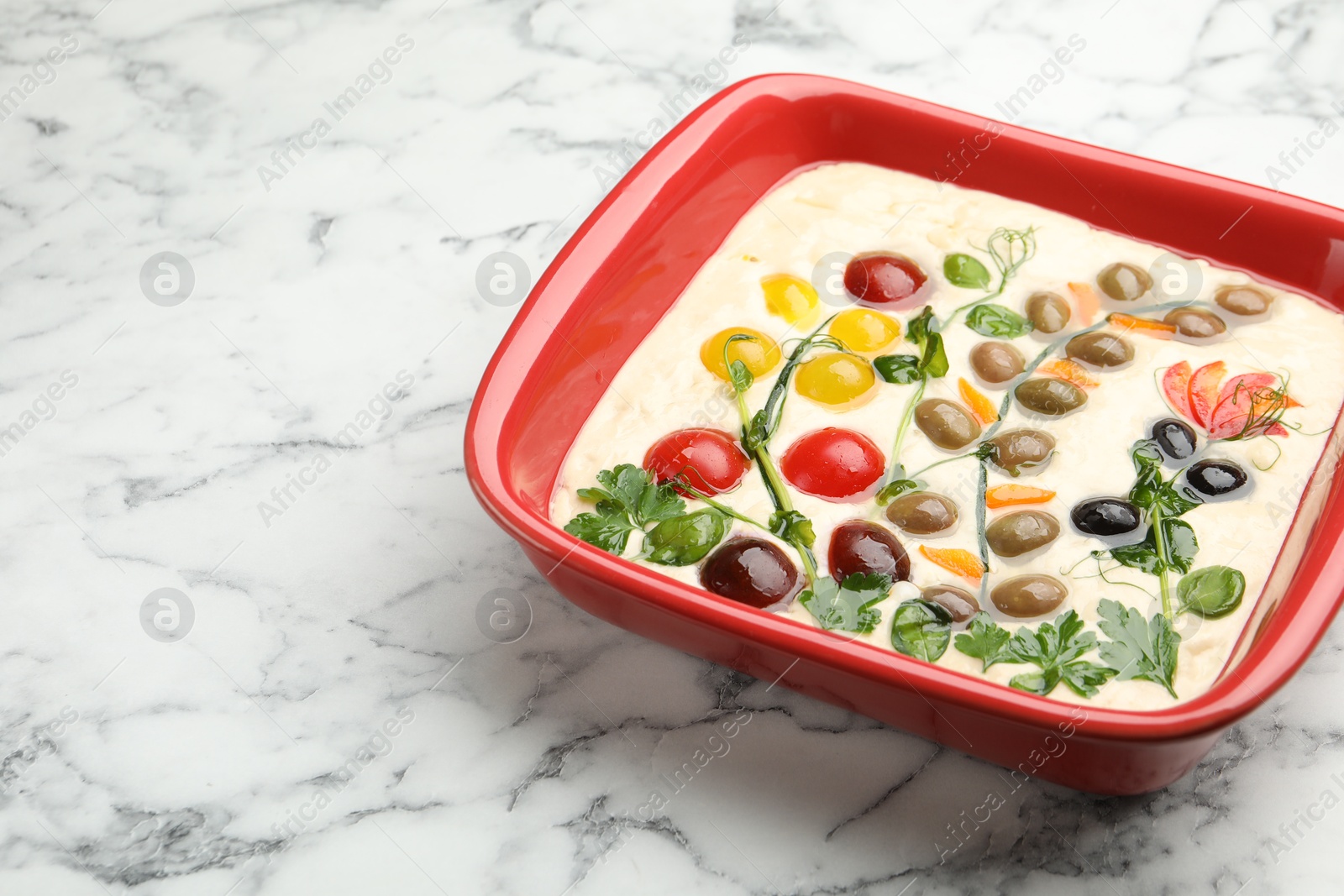 Raw focaccia with vegetables and olives in baking dish on white marble table, closeup Photo of Raw focaccia with vegetables and olives in baking dish on white marble table, closeup
